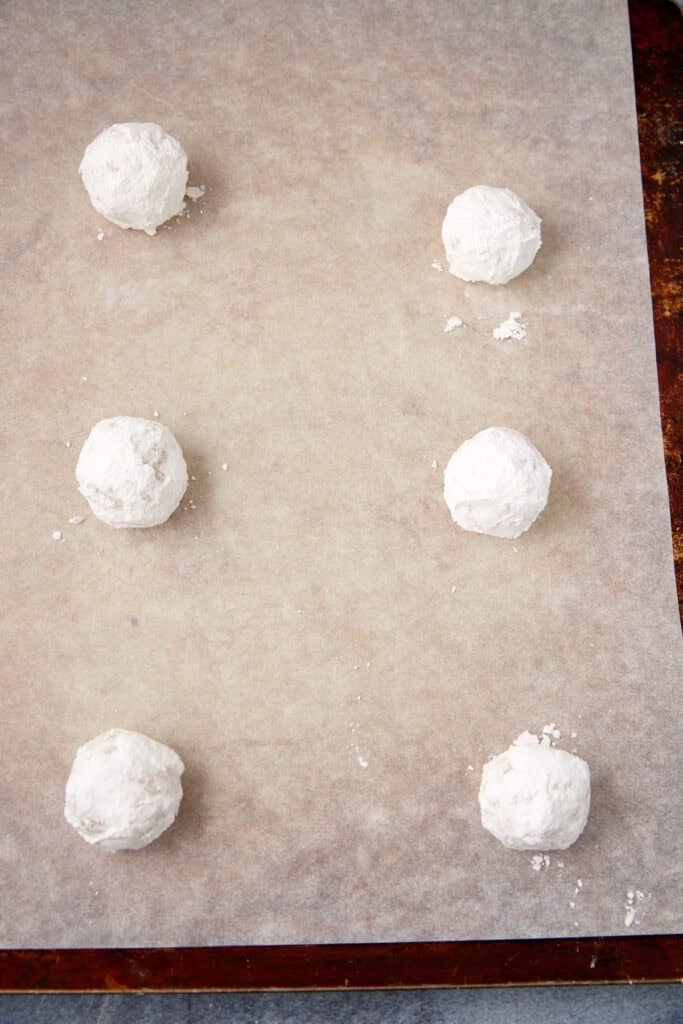Powdered sugar–coated lemon cookie dough balls spaced on a parchment-lined baking sheet.