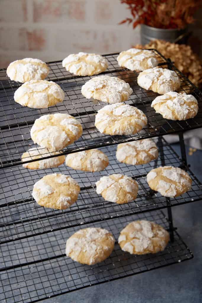 Lemon crinkle cookies cooling on wire racks with powdered sugar crackles and a soft, pale yellow center.