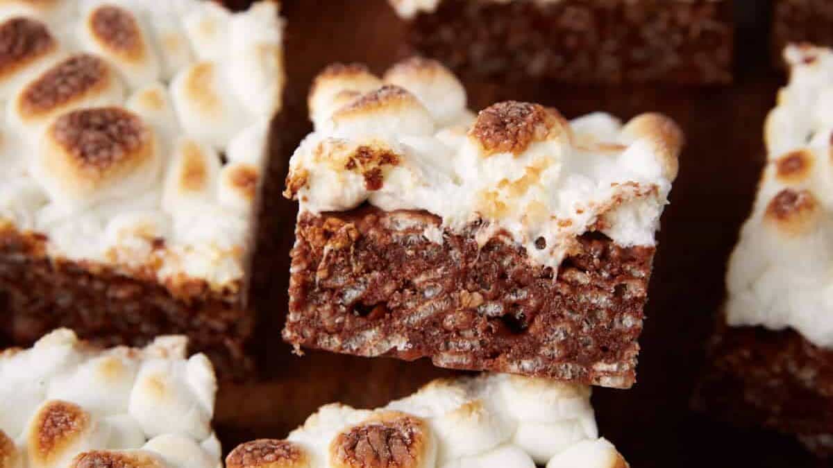 S&rsquo;mores bars cut into squares, one turned on its side to show the chocolate cereal layer under the toasted marshmallows.