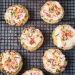 Close overhead of frosted sprinkle cookies on a cooling rack.