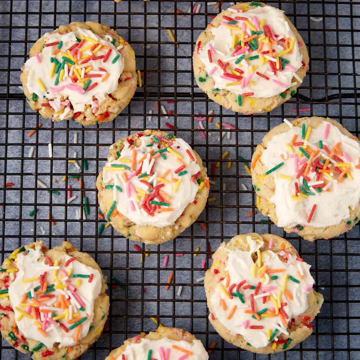 Close overhead of frosted sprinkle cookies on a cooling rack.