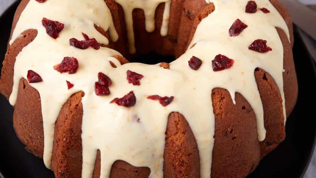 Cranberry orange bundt cake is glazed and topped with chopped dried cranberries on a serving plate.