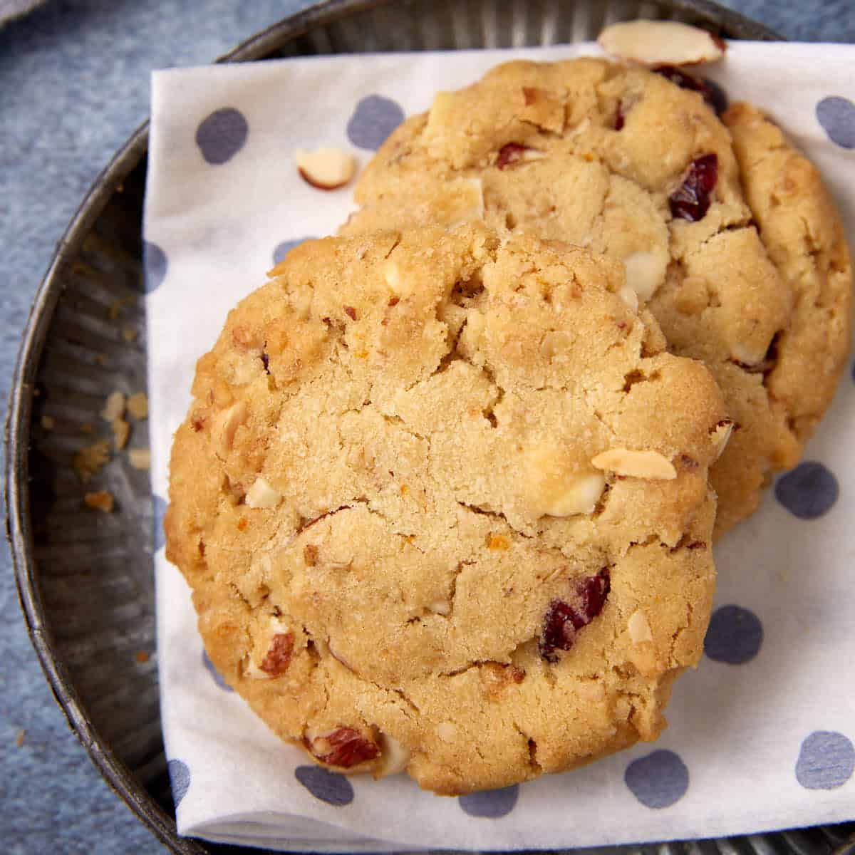 A close-up shows two cranberry orange cookies on a polka-dot napkin, highlighting the cracked tops and mix-ins.