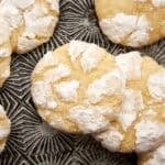 Overhead view of lemon crinkle cookies with crackly powdered sugar tops on a dark patterned plate.