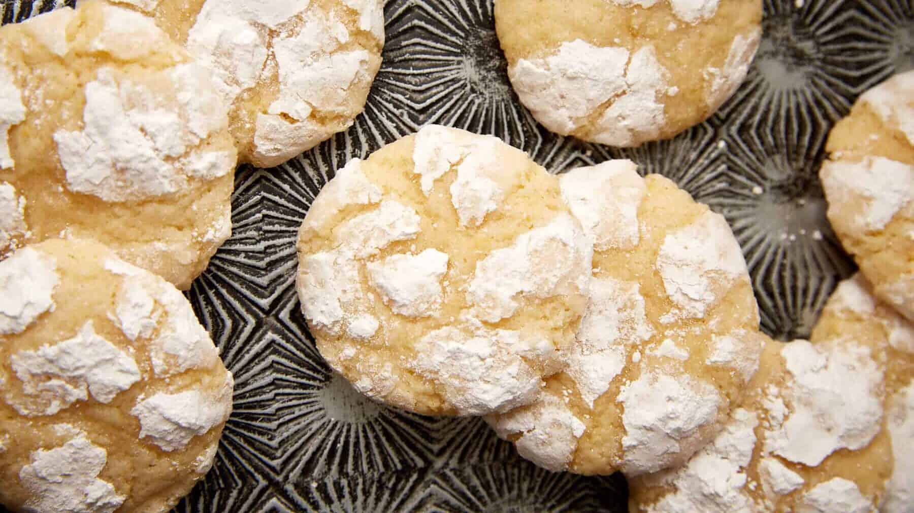 Overhead view of lemon crinkle cookies with crackly powdered sugar tops on a dark patterned plate.