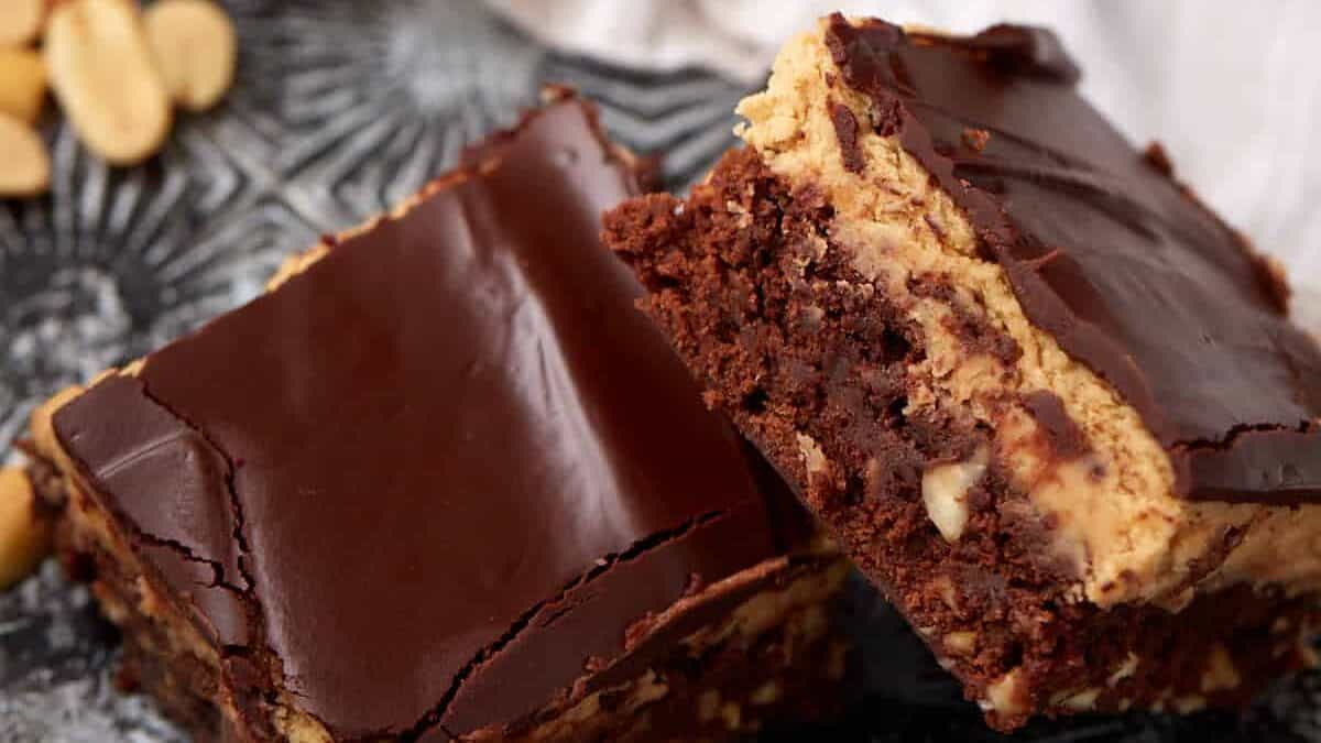 Close-up of sliced peanut butter brownies stacked on a plate, showing the fudgy brownie base, peanut butter layer, and glossy chocolate glaze.