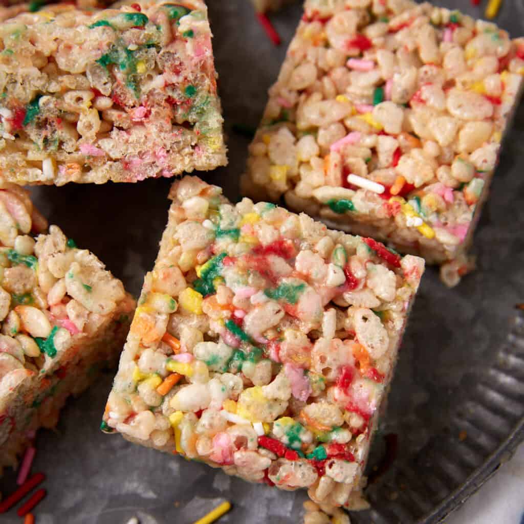 Close-up of a square Rice Krispie treat with colorful sprinkles on a dark plate.