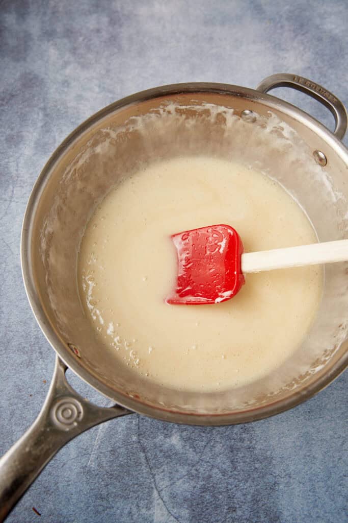 Melted marshmallow mixture in a saucepan stirred smooth with a red spatula.