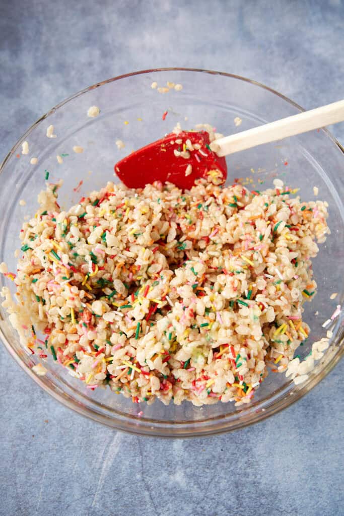Rice Krispie mixture stirred with melted marshmallows and sprinkles in a glass bowl.