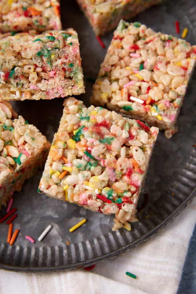 Rice Krispie treats with sprinkles on a dark plate, showing the soft center and colorful marshmallow coating.