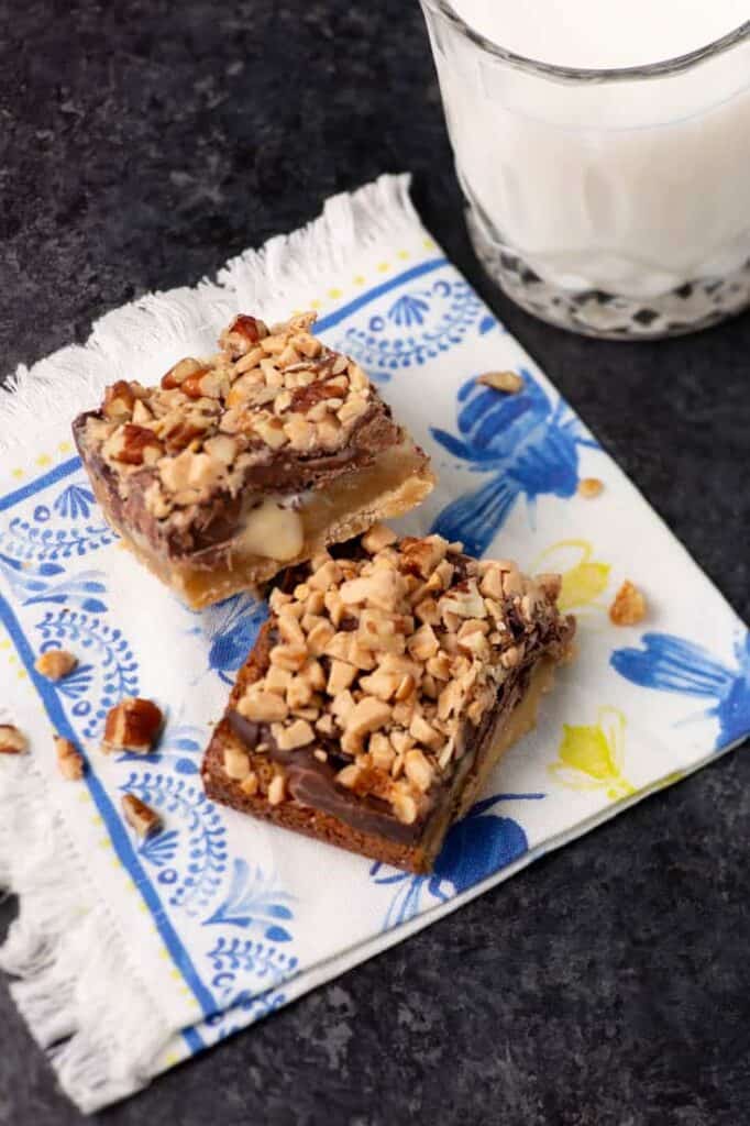 Two shortbread toffee bars on a patterned napkin beside a glass of milk.