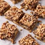 Shortbread toffee bars cut into squares with chocolate, toffee bits, and chopped pecans on top.