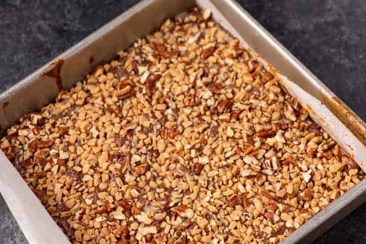 Baked shortbread toffee bars in a square pan topped with chopped pecans and toffee bits.