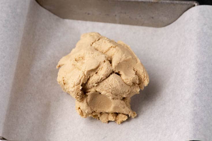 Shortbread dough pressed into a square parchment-lined baking pan before baking.