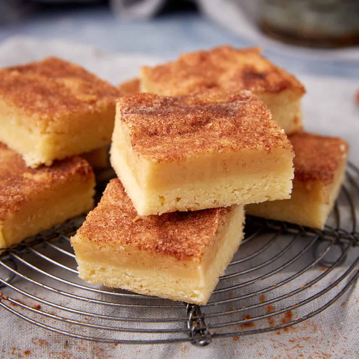 Layered snickerdoodle bars stacked on a cooling rack with a cinnamon sugar top.