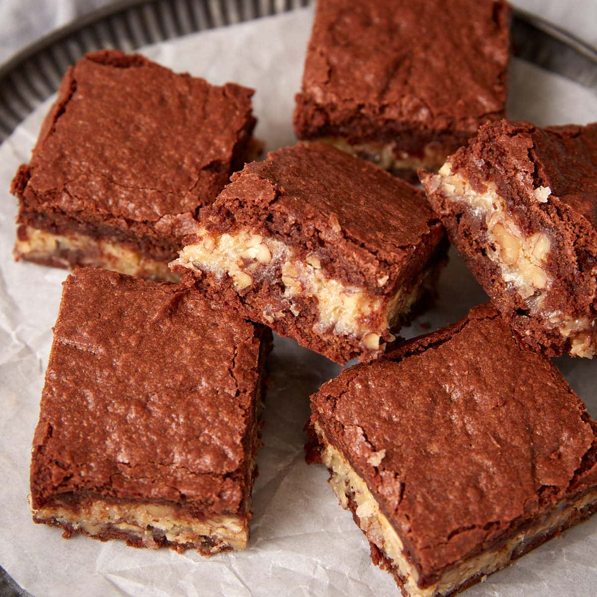 German chocolate brownies stacked on a plate, showing the coconut pecan filling between the brownie layers.