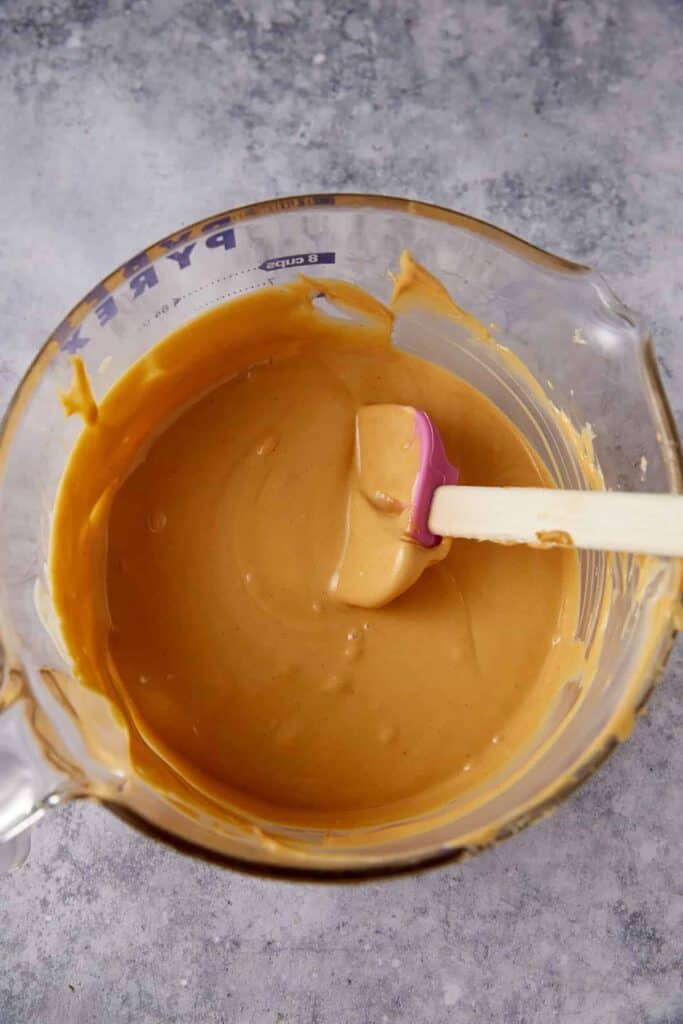 Melted white chocolate and butterscotch mixture stirred with peanut butter in a glass measuring bowl.
