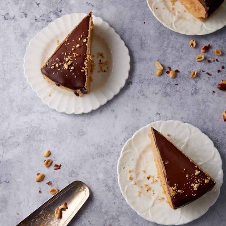 Overhead view of two slices of peanut butter pie with chocolate topping on white plates with a pie server nearby.