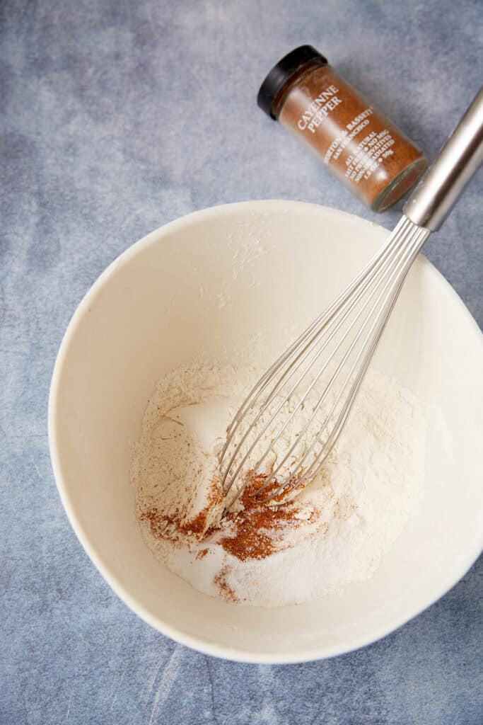Dry ingredients for peppery peanut butter cookies whisked together in a white mixing bowl with cayenne pepper nearby.