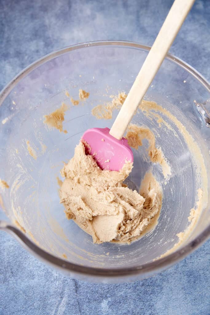 Ingredients for peppery peanut butter cookies arranged on a blue surface, including flour, sugars, peanuts, peanut butter, butter, egg, vanilla, baking soda, and cayenne.