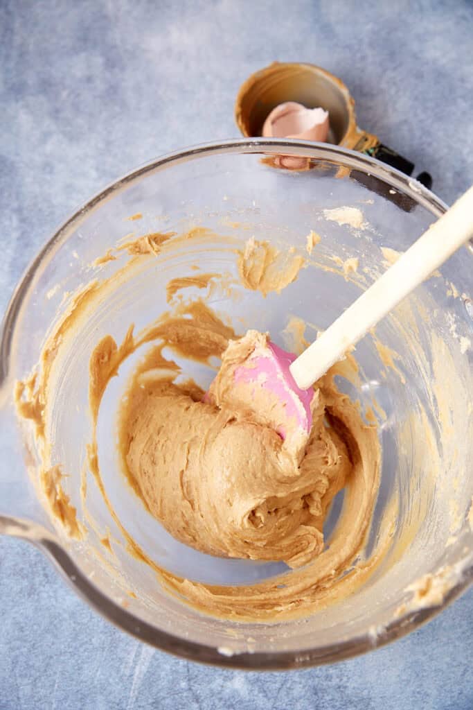 Peanut butter cookie dough mixed in a glass bowl with a pink spatula.
