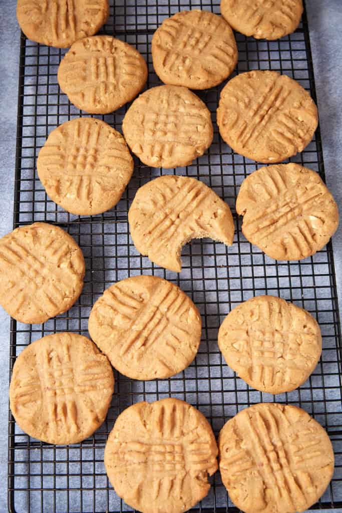 Peppery peanut butter cookies on a wire rack with one cookie missing a bite.