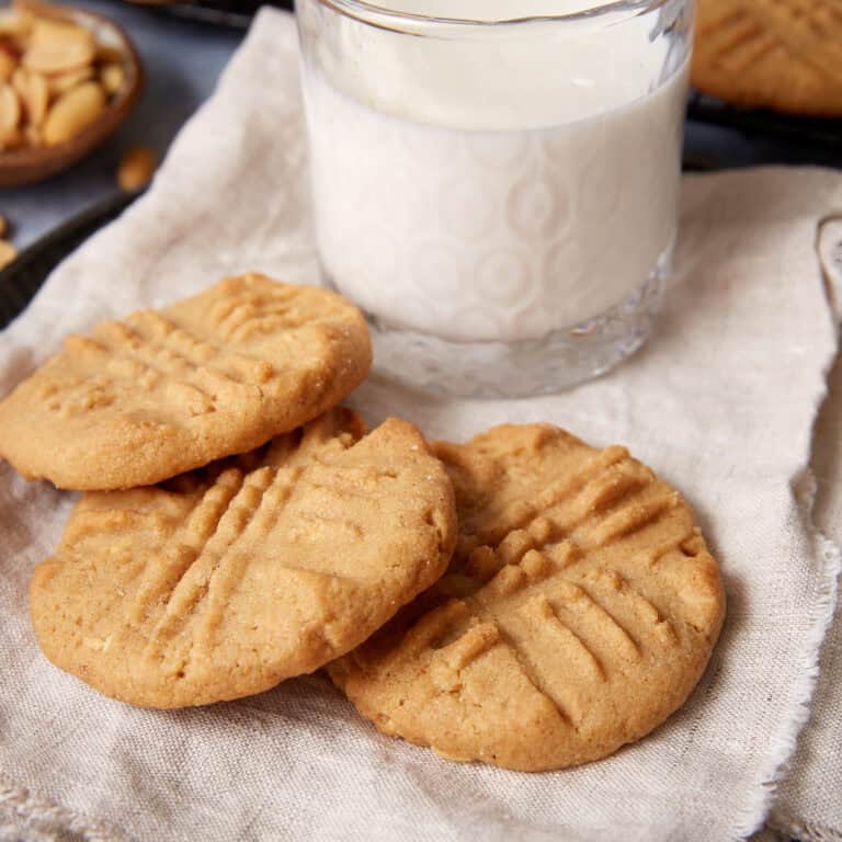 Three peppery peanut butter cookies on a linen napkin with a glass of milk behind them.