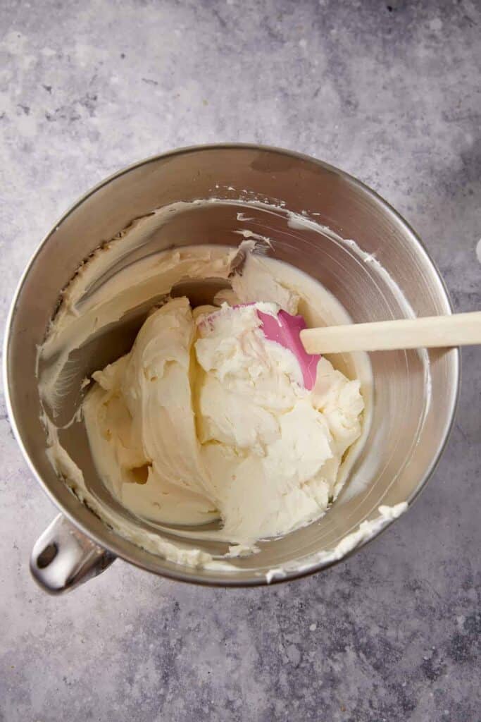 Cream cheese beaten smooth in a stand mixer bowl with a spatula for pumpkin pie cheesecake bars.