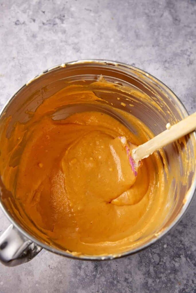 Pumpkin cheesecake batter mixed until smooth in a stand mixer bowl with a spatula.