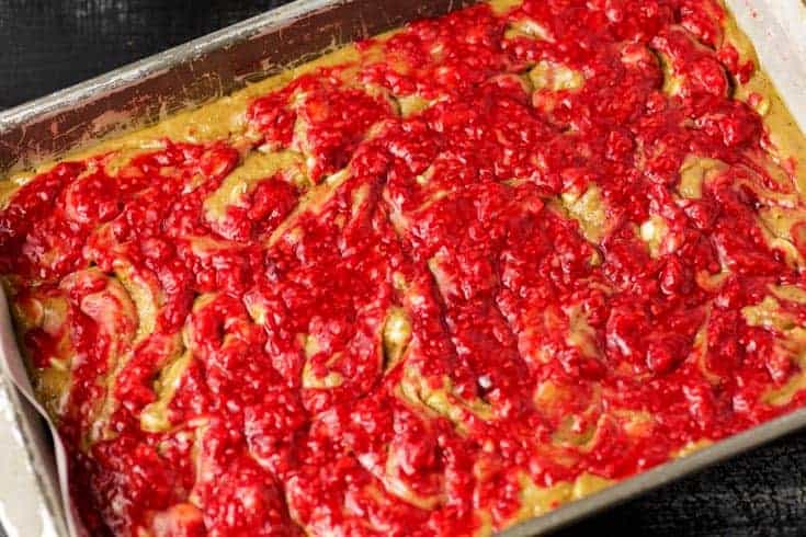Raspberry white chocolate blondie batter spread in a parchment-lined baking pan with bright raspberry swirl on top before baking.
