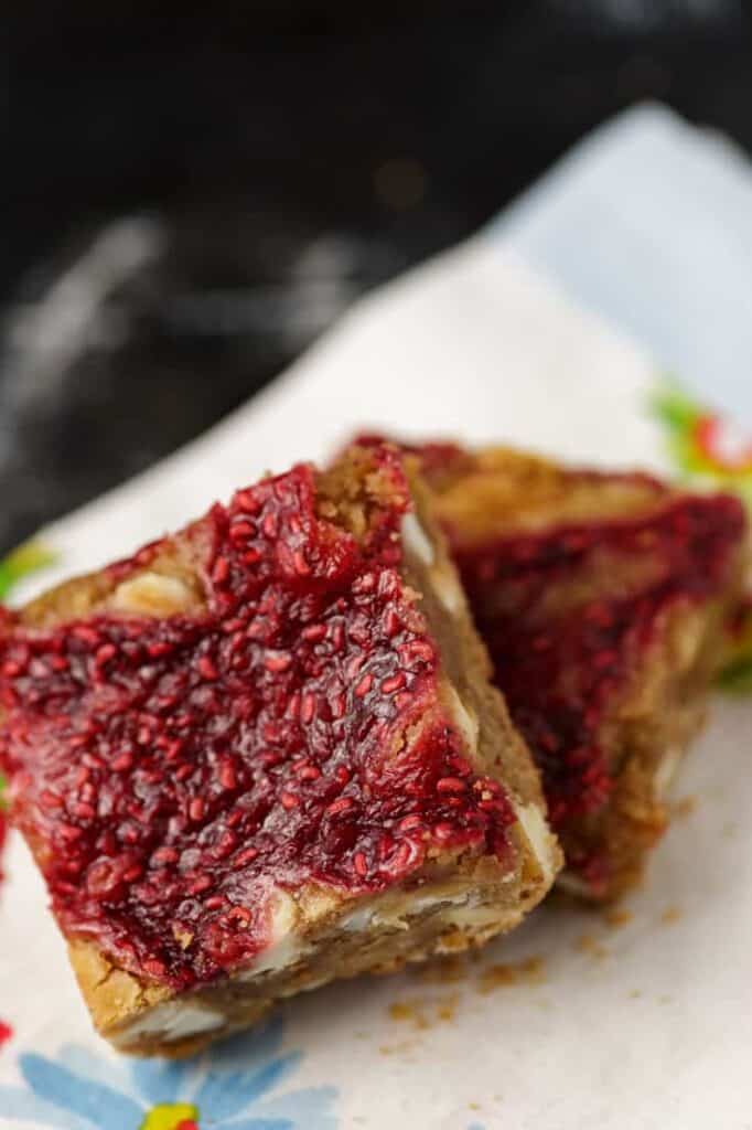 Two raspberry white chocolate blondie bars stacked on a plate, showing gooey white chocolate and raspberry swirls.