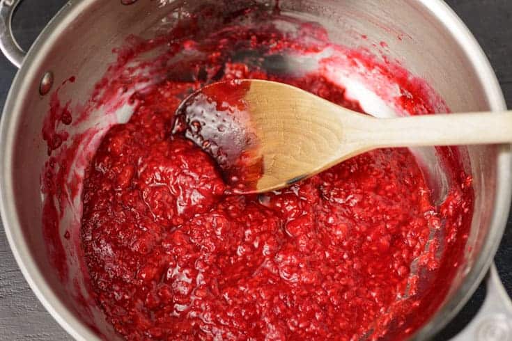 Homemade raspberry sauce cooked down in a saucepan with a wooden spoon.
