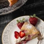 Close-up of strawberry lemon cake with whipped cream, fresh strawberries, and a bite on a fork.