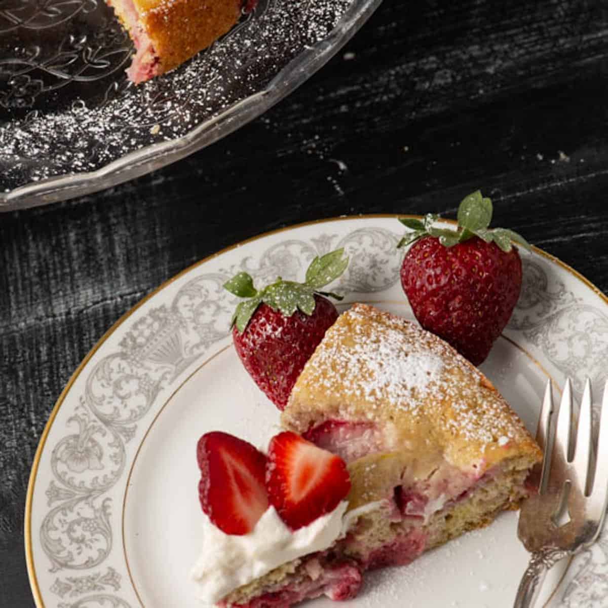 Close-up of strawberry lemon cake with whipped cream, fresh strawberries, and a bite on a fork.