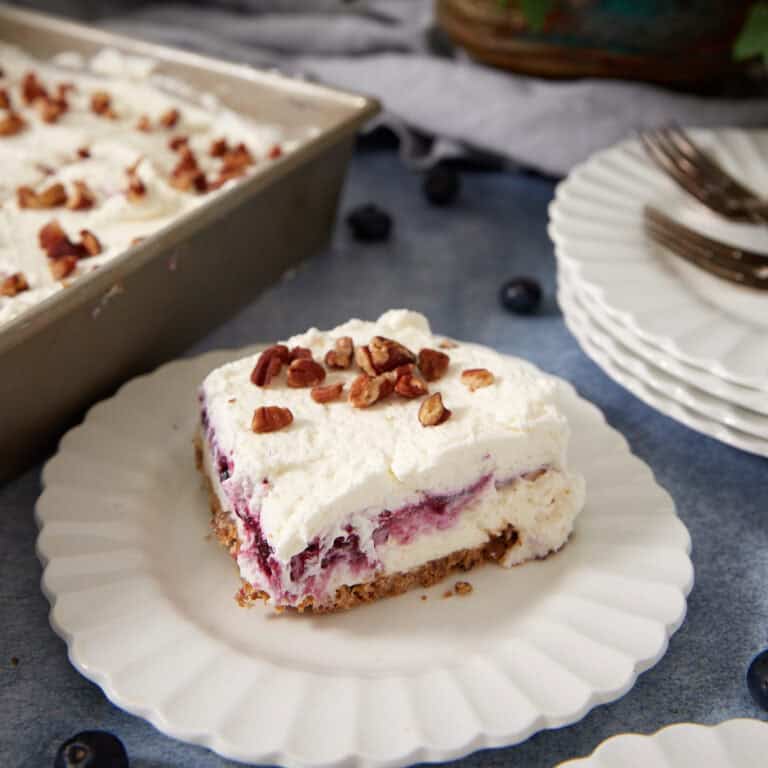 Slice of Blueberry Yum Yum on a white plate with whipped cream, blueberry filling, shortbread crust, and toasted pecans.