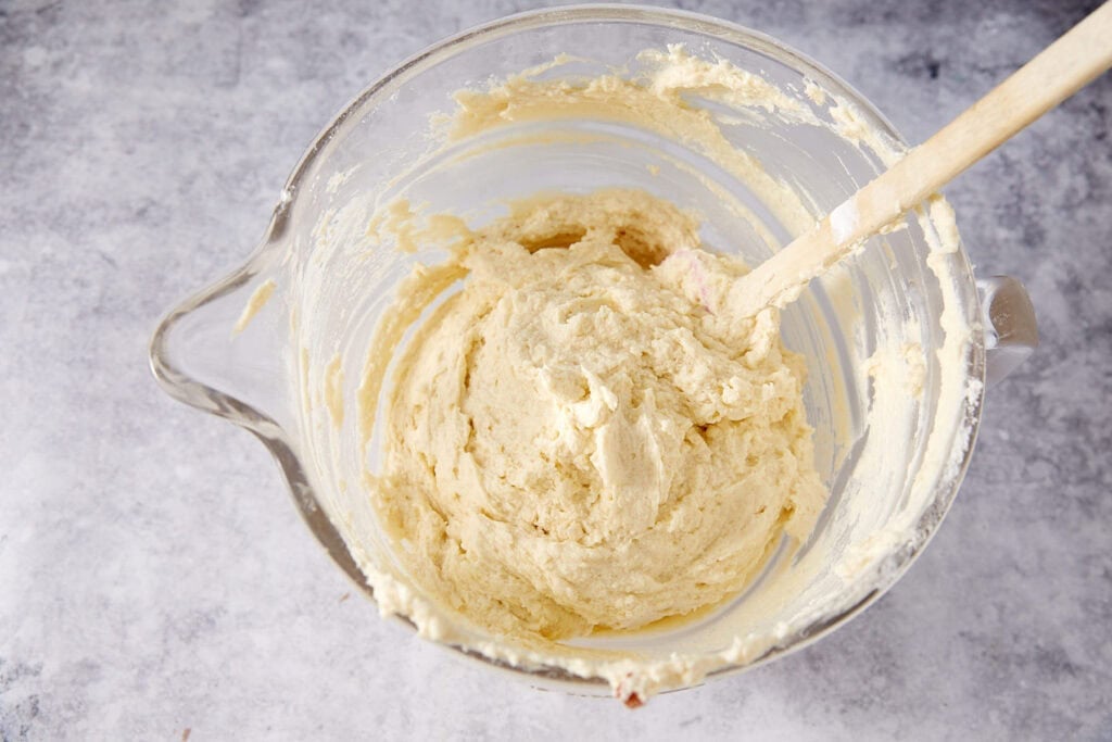 Completed honey bun cake batter in a glass mixing bowl, thick and smooth, with a spatula resting inside.