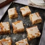 Several honey bun cake squares arranged on a dark patterned tray with white plates and a fork in the background.
