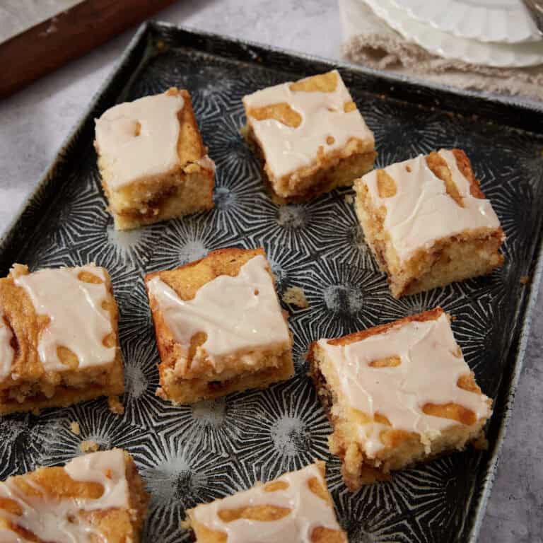 Several honey bun cake squares arranged on a dark patterned tray with white plates and a fork in the background.