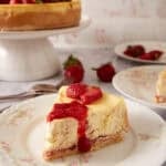 Slice of strawberry swirl cheesecake with strawberry sauce and fresh berries on a floral plate.