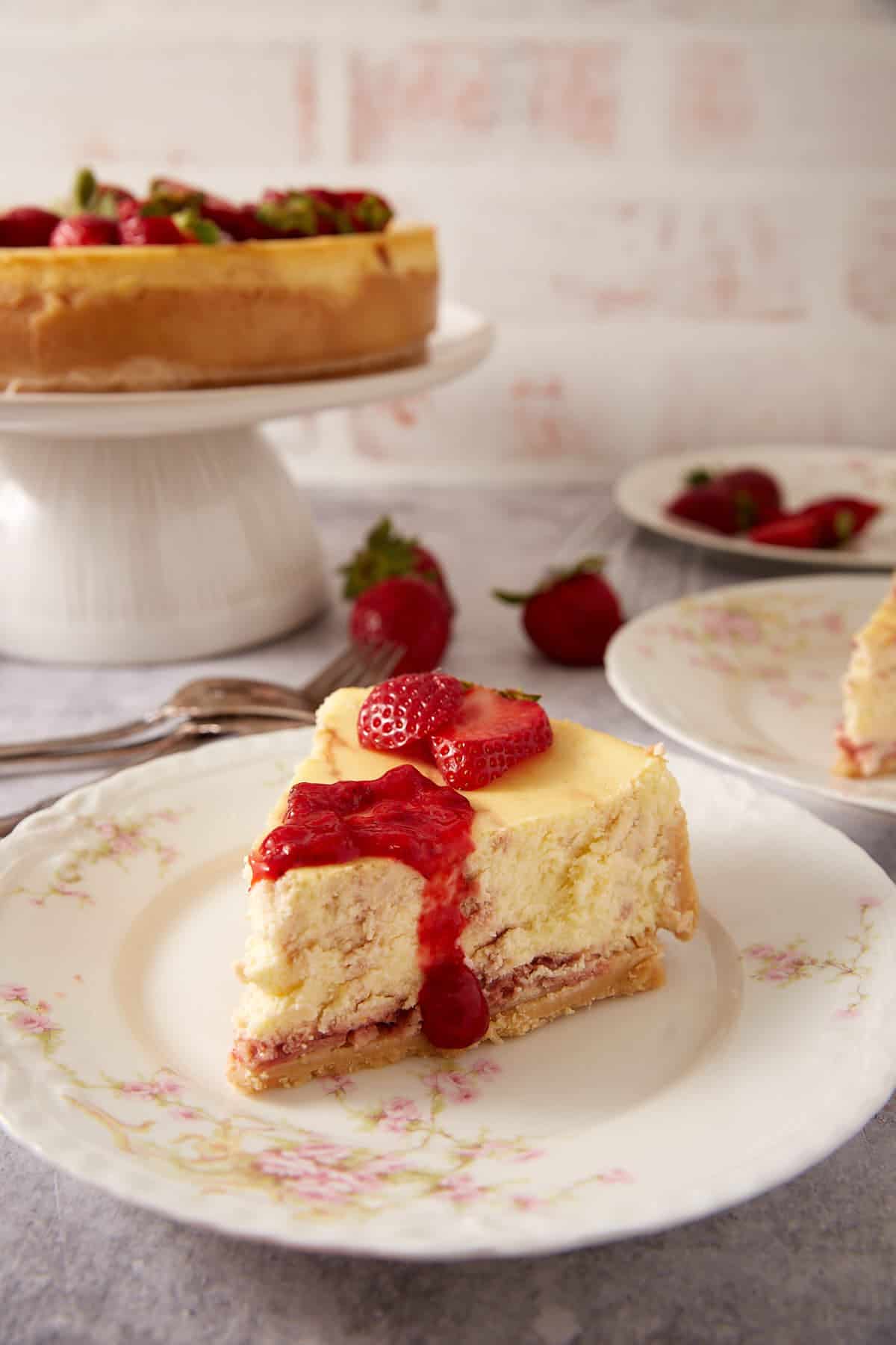 Slice of strawberry swirl cheesecake with strawberry sauce and fresh berries on a floral plate.