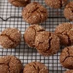 Sugar-coated molasses crinkle cookies on a black wire rack, crackled across the tops with the chewy interior visible in the cracks.