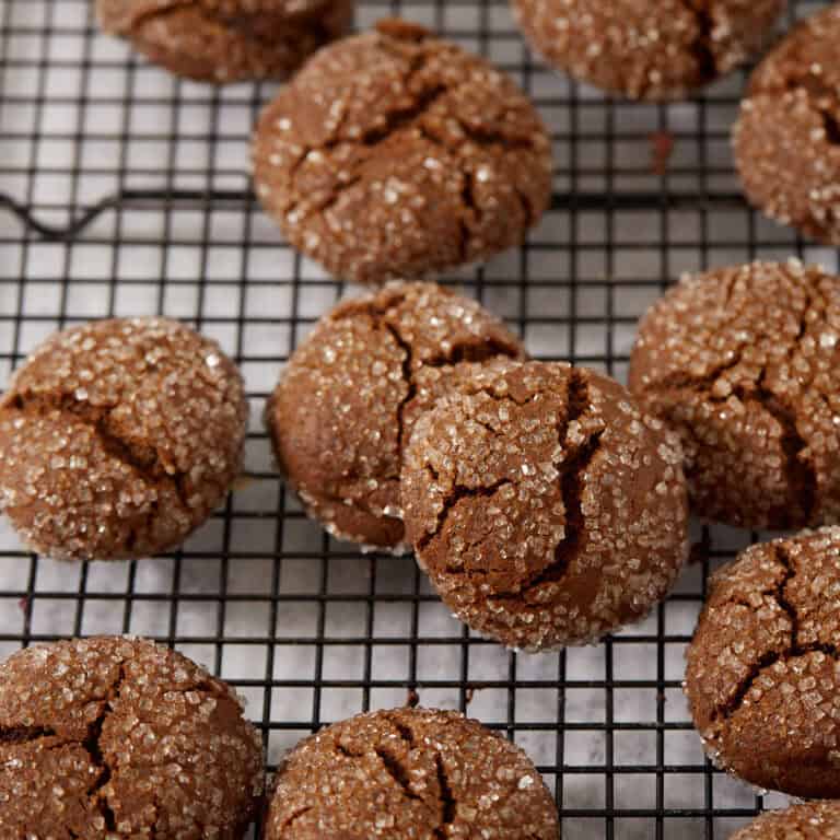 Sugar-coated molasses crinkle cookies on a black wire rack, crackled across the tops with the chewy interior visible in the cracks.
