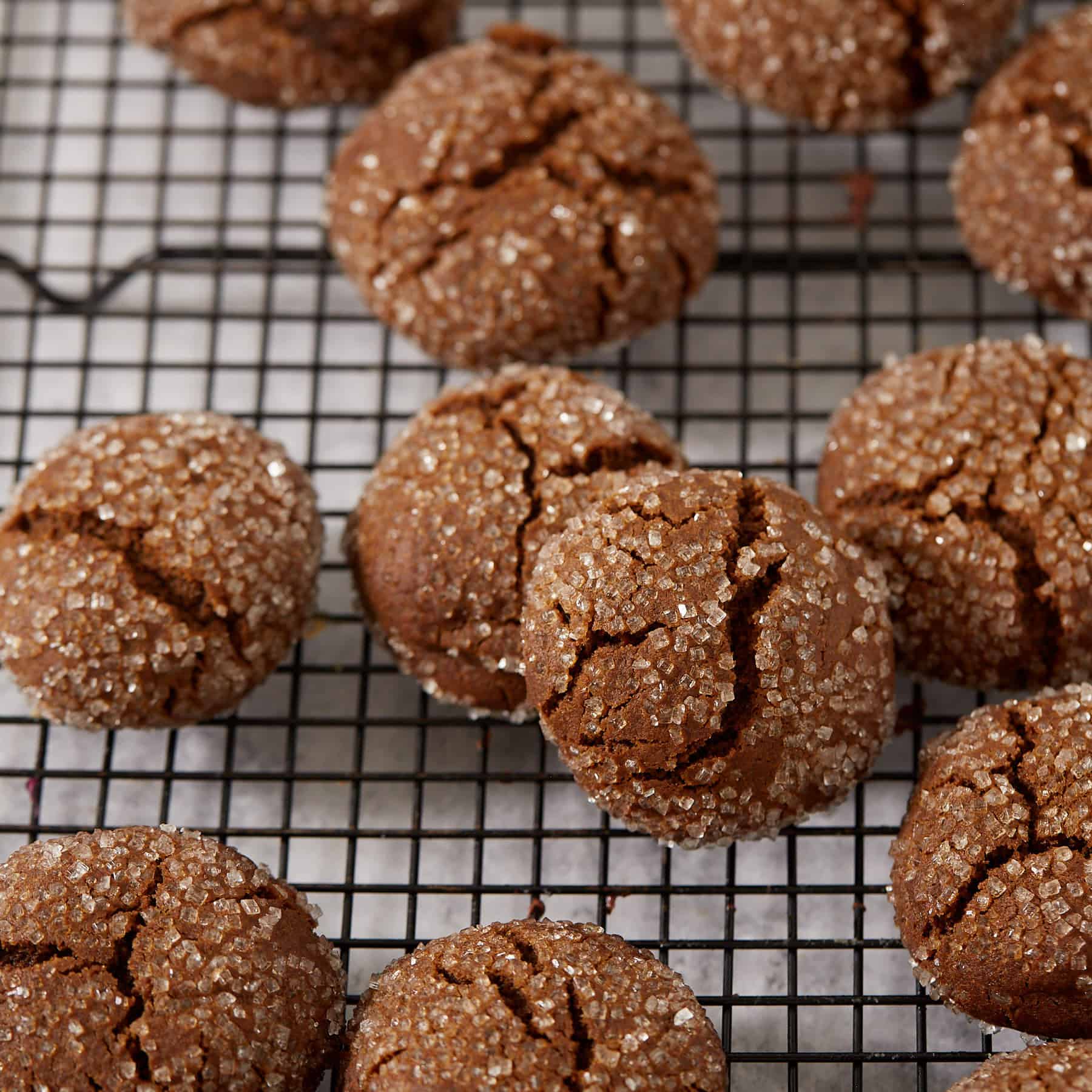 Sugar-coated molasses crinkle cookies on a black wire rack, crackled across the tops with the chewy interior visible in the cracks.