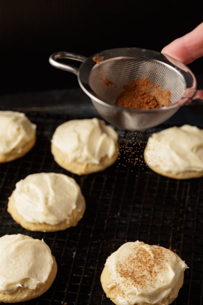 Cinnamon being sprinkled on top of the eggnog frosting.