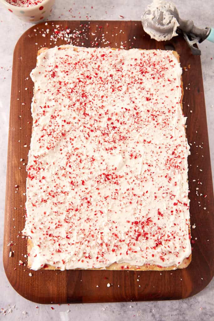 Rectangular sheet cake topped with white frosting and crushed peppermint candy on a wooden serving board.
