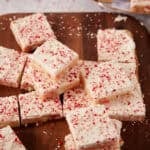 Square sugar cookie bars topped with white frosting and crushed peppermint candy on a wooden board.