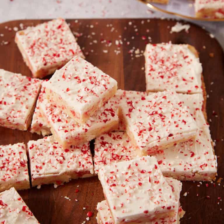 Square sugar cookie bars topped with white frosting and crushed peppermint candy on a wooden board.