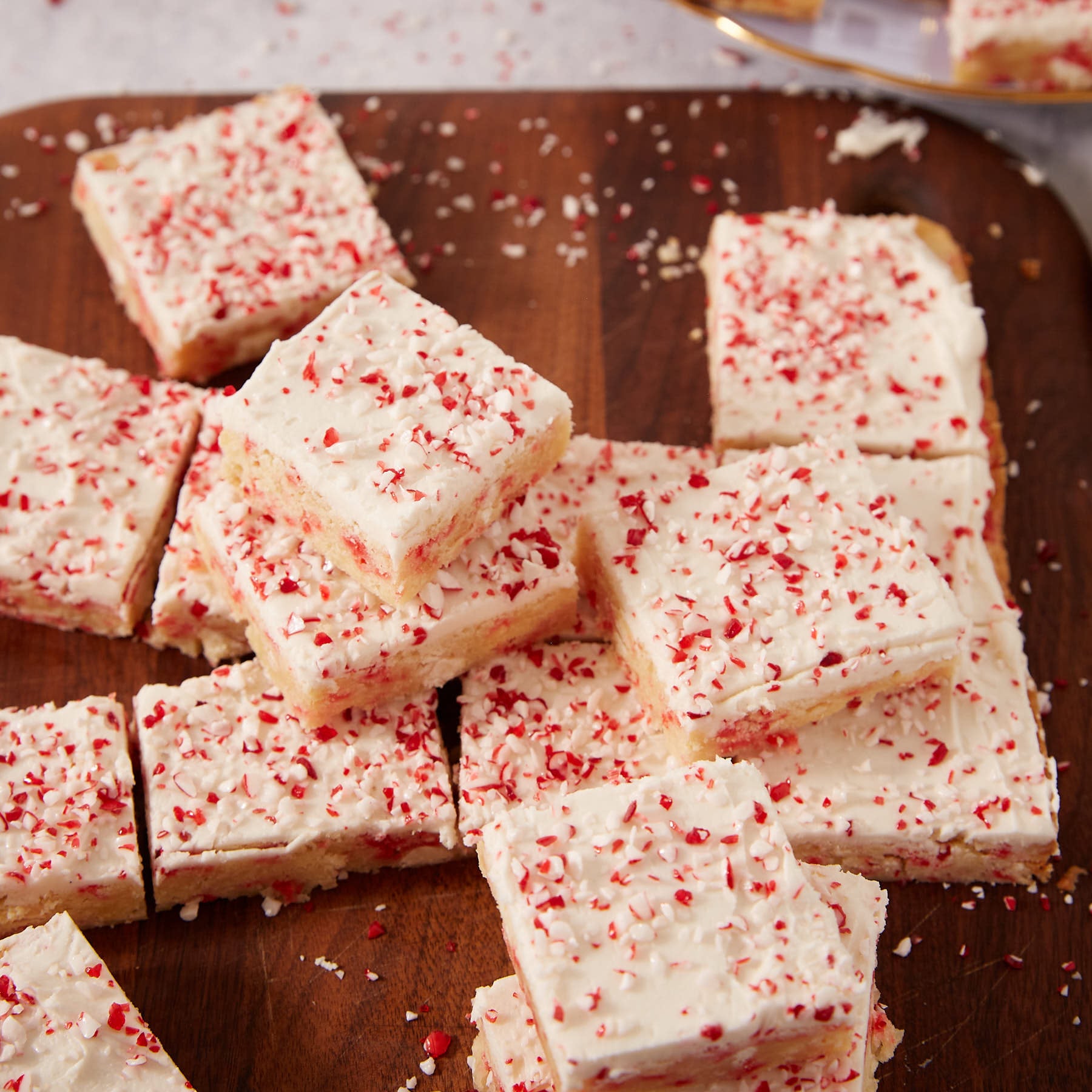 Square sugar cookie bars topped with white frosting and crushed peppermint candy on a wooden board.