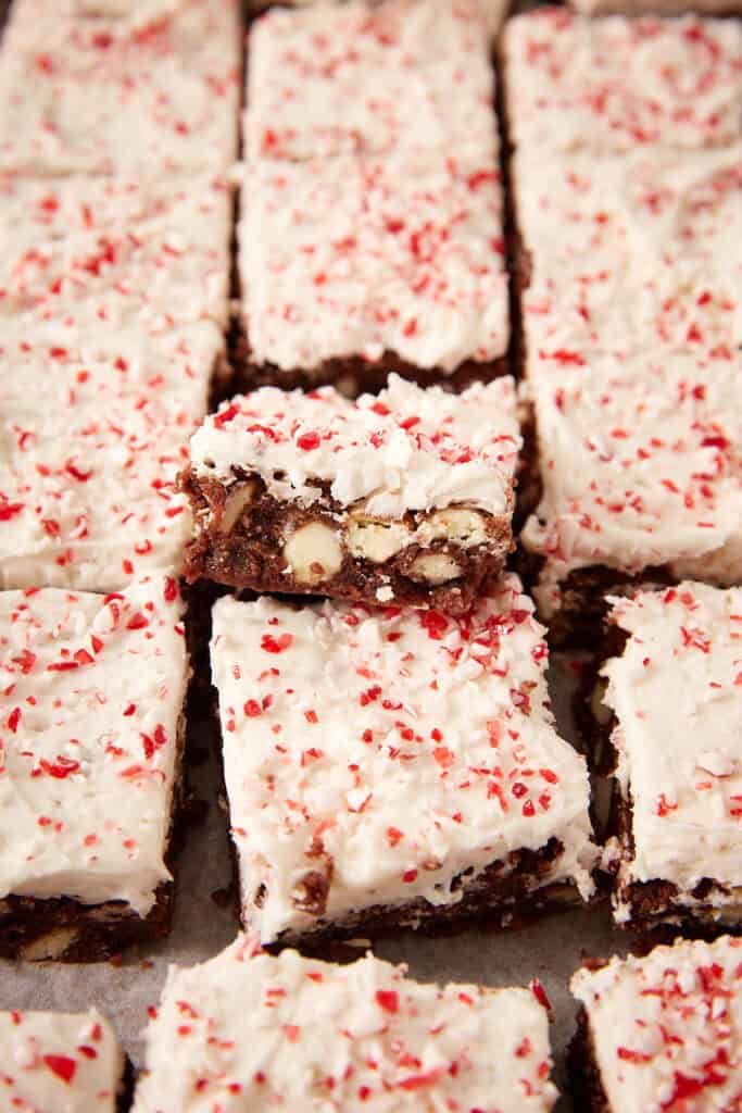 A batch of chocolate brownies topped with white frosting and crushed peppermint pieces.