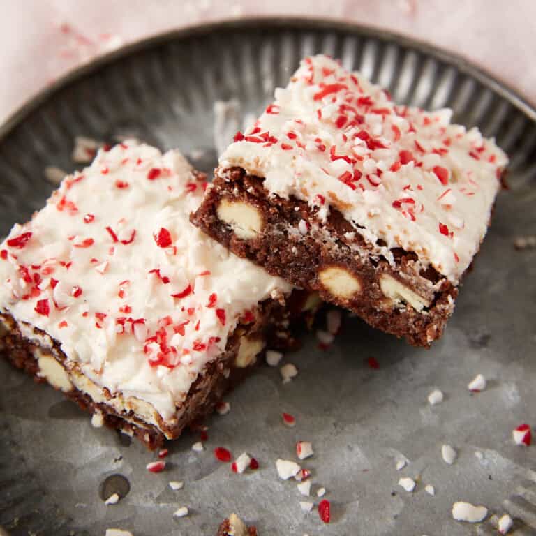 Two chocolate brownies topped with white frosting and crushed peppermint candy on a metal plate.